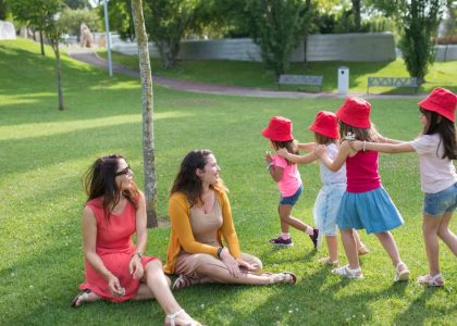 Happy children playing in a sunny park with two mothers sitting nearby, enjoying the outdoors.