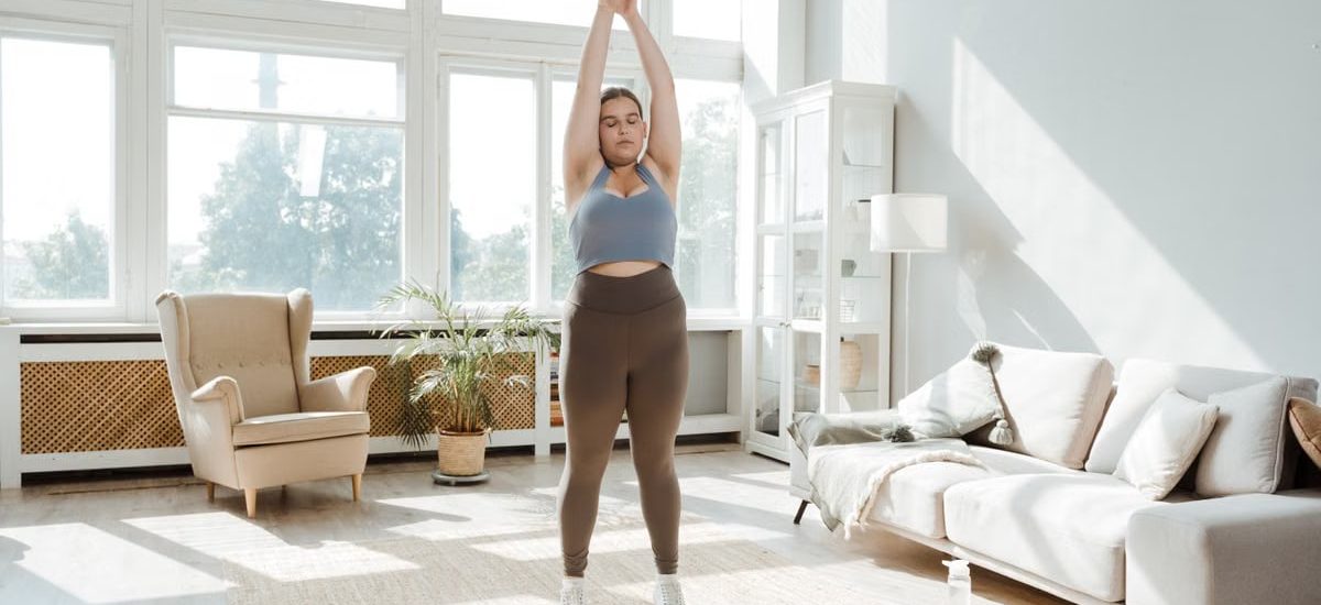 A woman practices stretching exercises in a sunlit living room, promoting wellness and healthy lifestyle.